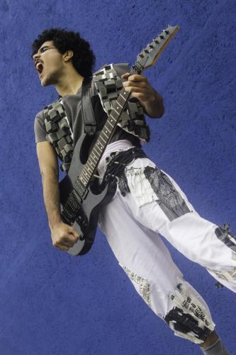 Ator vestido com o figurino do espetáculo O mundo de tludi carregando uma guitarra